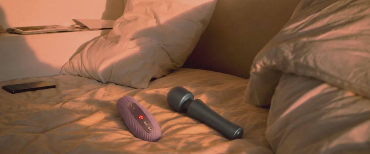 Palm-shaped vibrator and handled mini wand beside water-based lubricant on a bedside table.