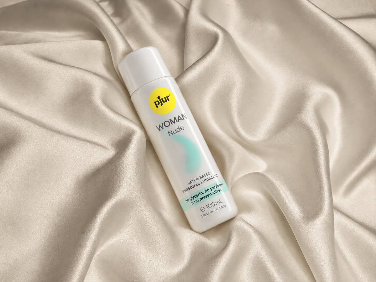 Water-based lubricant and soft intimate-care accessories arranged on elegant cream and muted-plum fabric