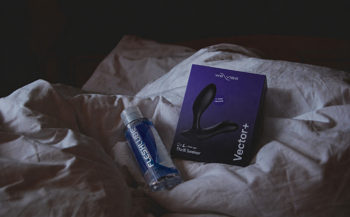 Curved prostate massager beside water-based lubricant on soft neutral fabric.