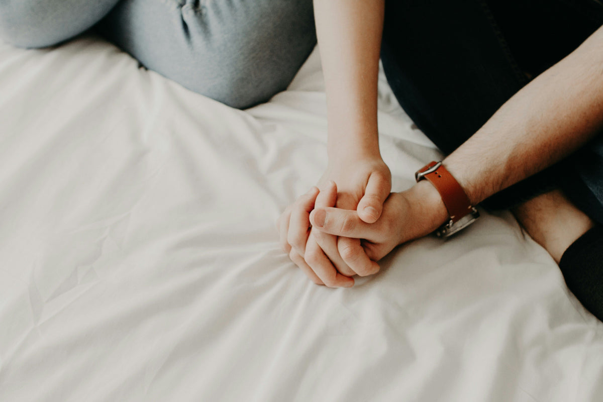 Couple holding hands on a bed beside a compact vibrator and water-based lubricant.
